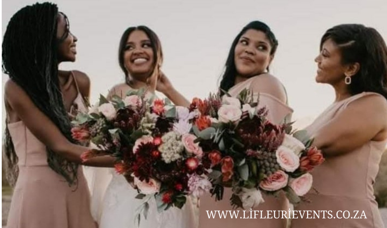 Bridesmaids in blush dresses holding deep red and pink bouquets