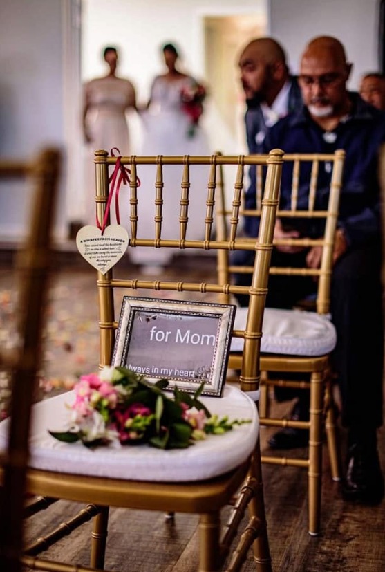 Gold ceremony chair reserved for Mom with a framed sign and flowers on the seat