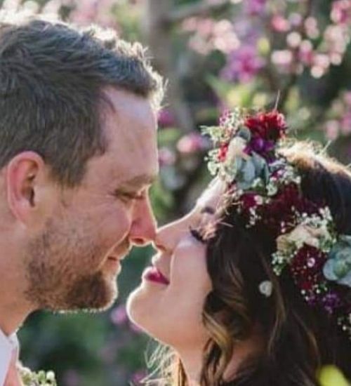 Bride in a red and pink flower crown smiling face to face with the groom