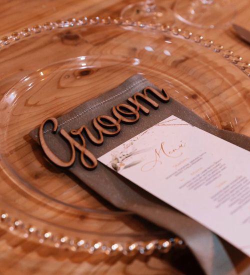 Groom place setting with a wooden name sign, menu and grey ribbon