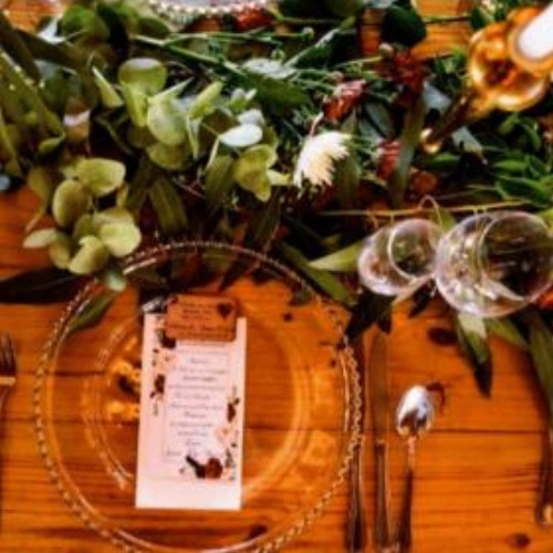 Wooden table with greenery runner, floral menu card and glass charger plate